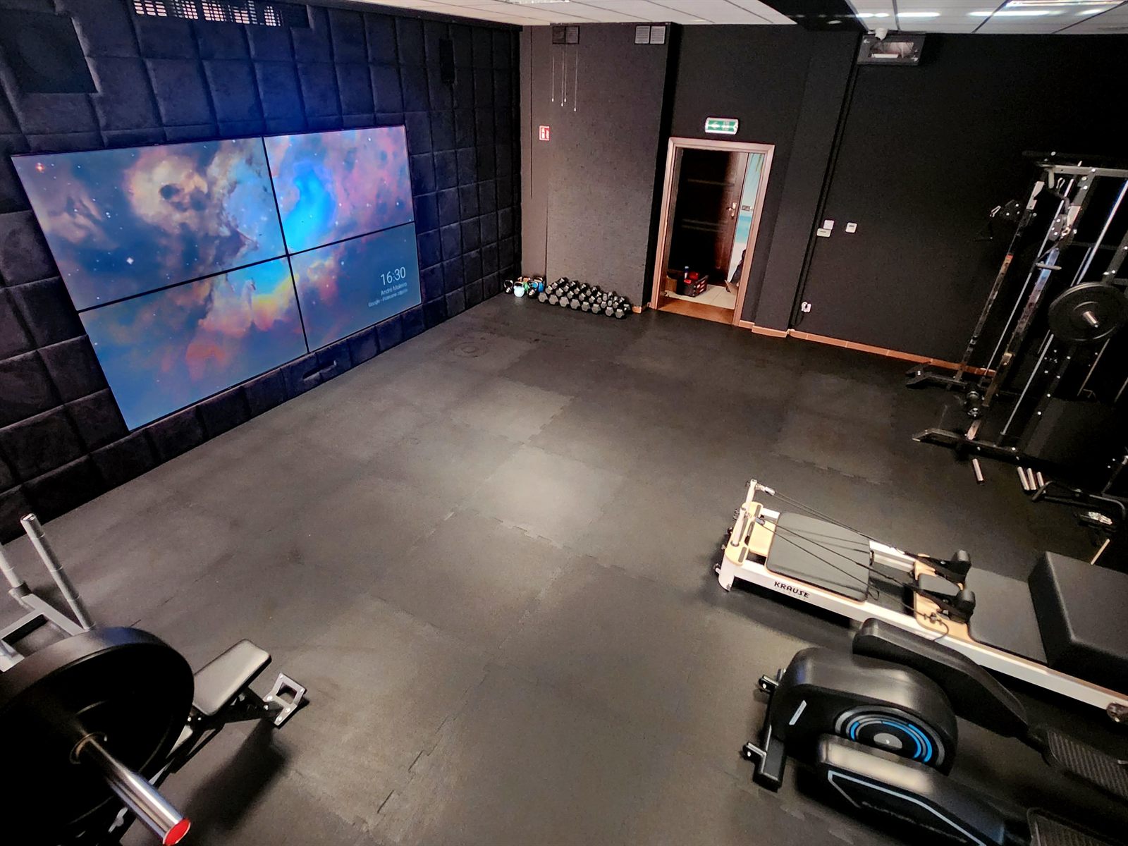Główna sala BodyTop Studio — ściana wideo z czterech ekranów, rząd hantli przy wejściu, brama wielofunkcyjna, wioślarz i reformer Krause